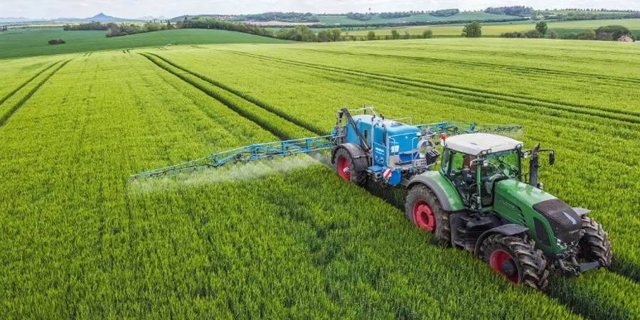 This picture shows a crop sprayer in action, spraying water on crops across a farm field, demonstrating the essential role of agricultural machinery in crop maintenance and precision farming.